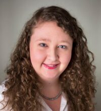Dr. Lindsey Ogle smiles while wearing a white top in front of a neutral background.