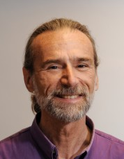 Dr. John McGrew smiles at the camera in front of a neutral background wearing a red shirt.