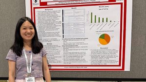 A COMPASS student stands in front of a poster at a conference and smiles at the camera