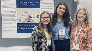 Three COMPASS students stand in front of a poster titled, "Promoting Teacher Well-Being" at a conference.