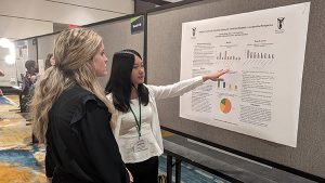A COMPASS student discusses a poster at a conference to a patron.