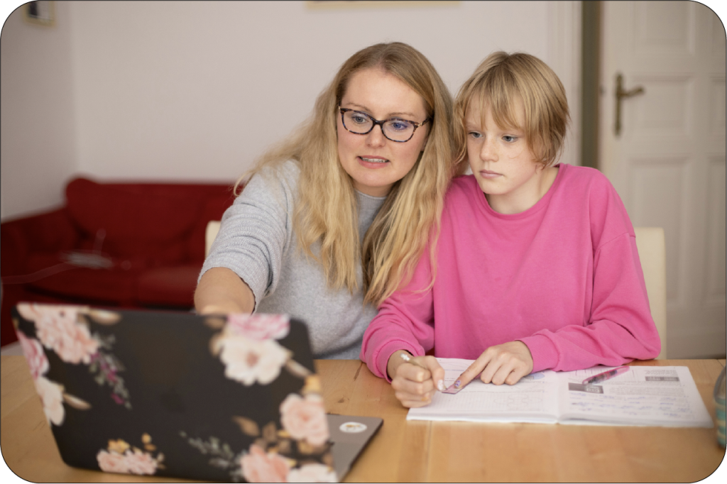 A teacher works with a student on an assignment using paper and a laptop with a floral cover.